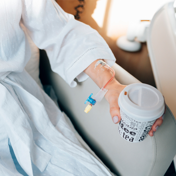 Person receiving IV drip therapy while holding a coffee cup