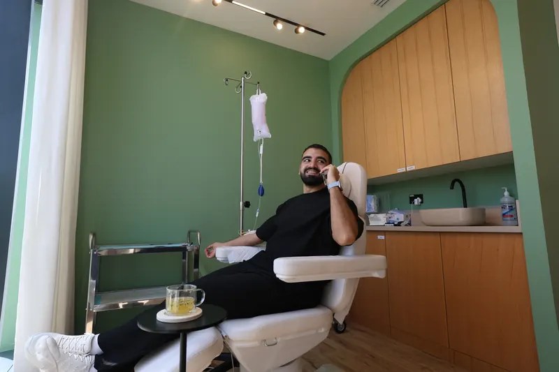 A client on a phone call during an intravenous drip session in a treatment room