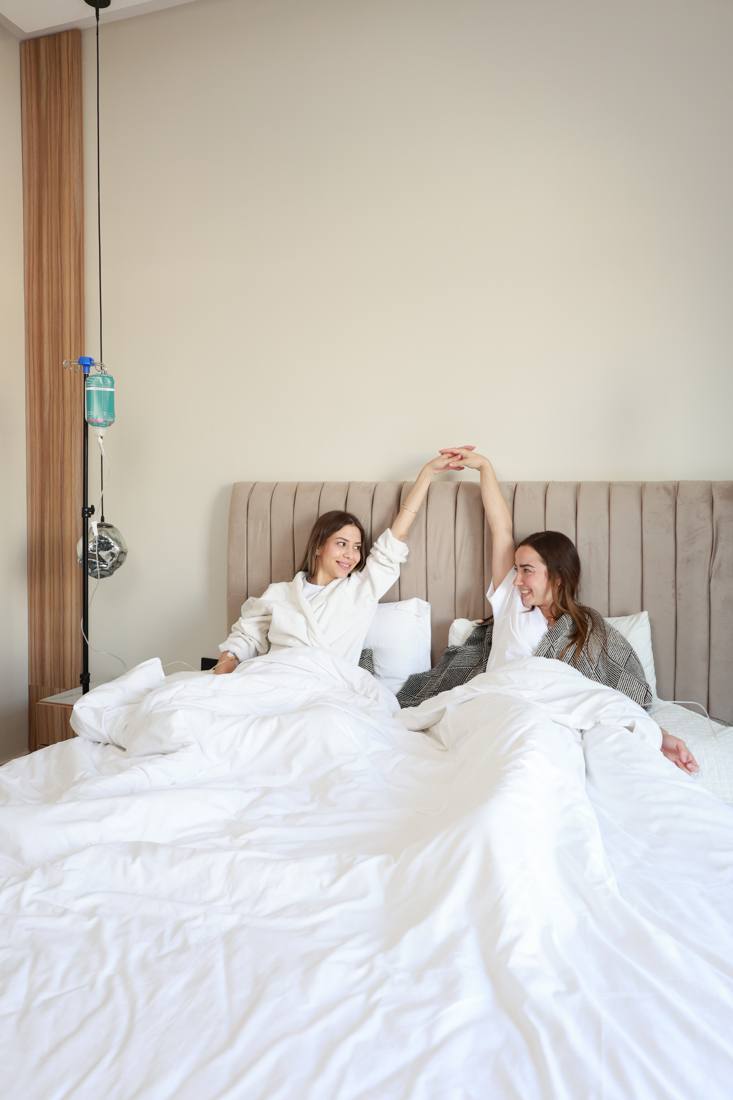 Two clients relaxing in bed at home while receiving IV drips